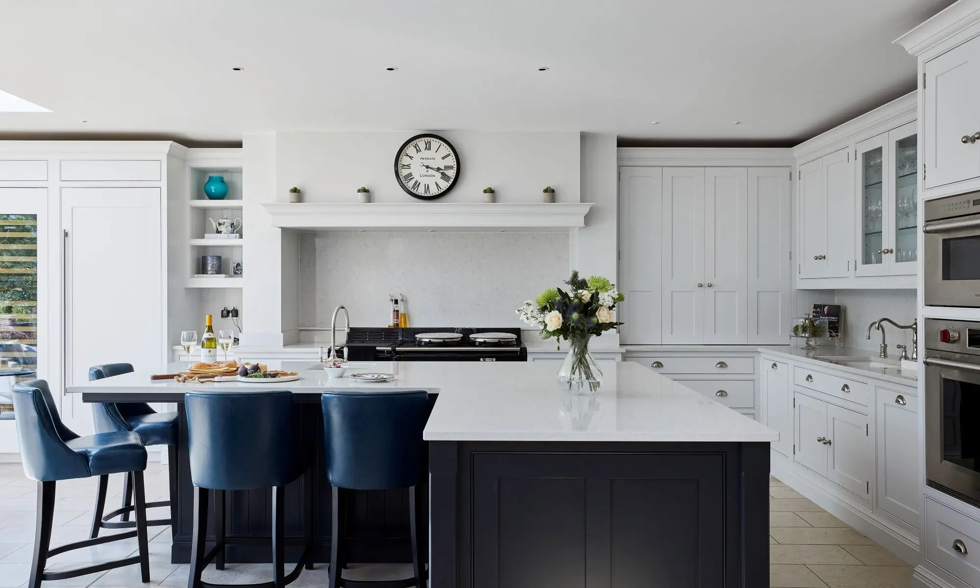 A white kitchen with blue chairs and a clock.