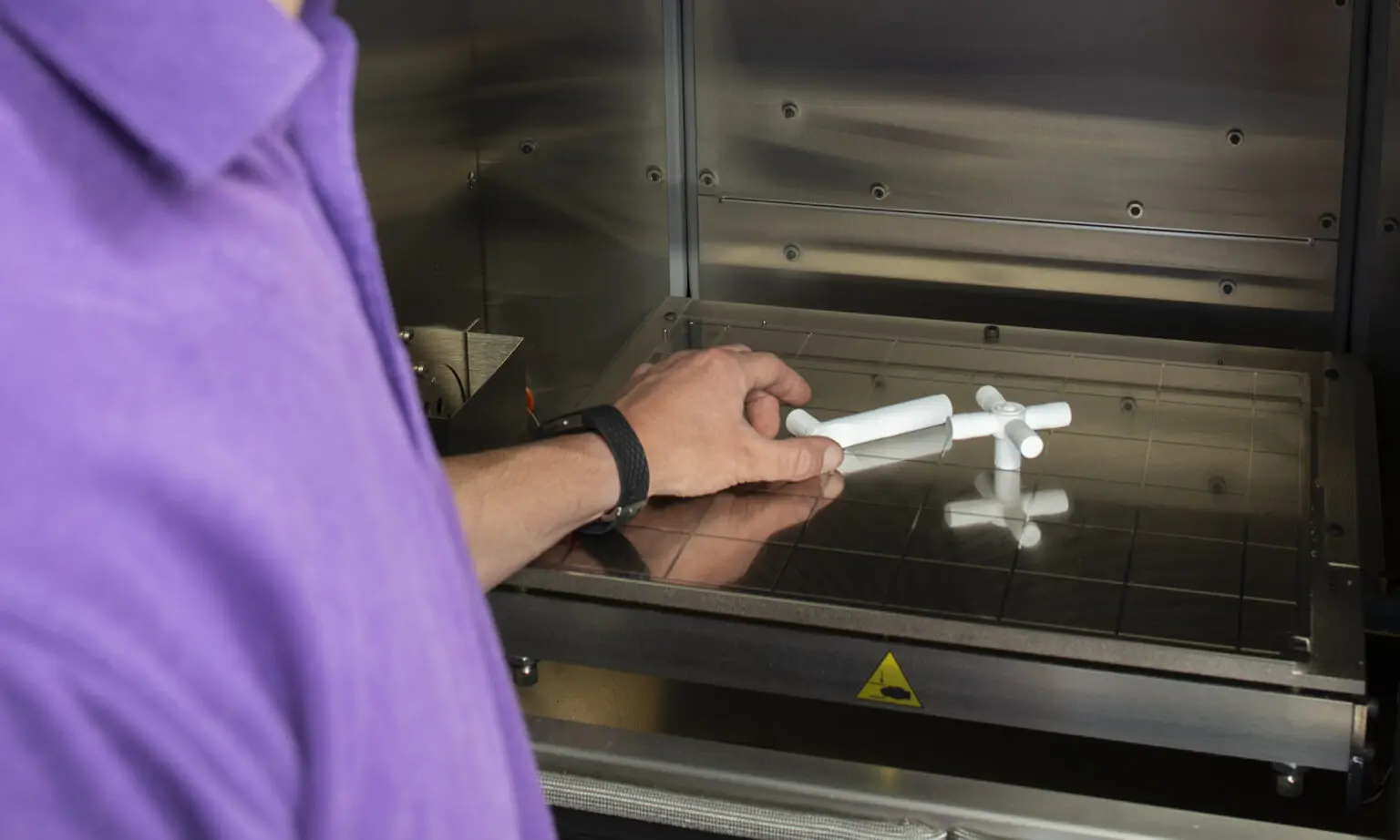A manufacturing engineer picks up 3D prototypes from inside a carbon fiber machine.