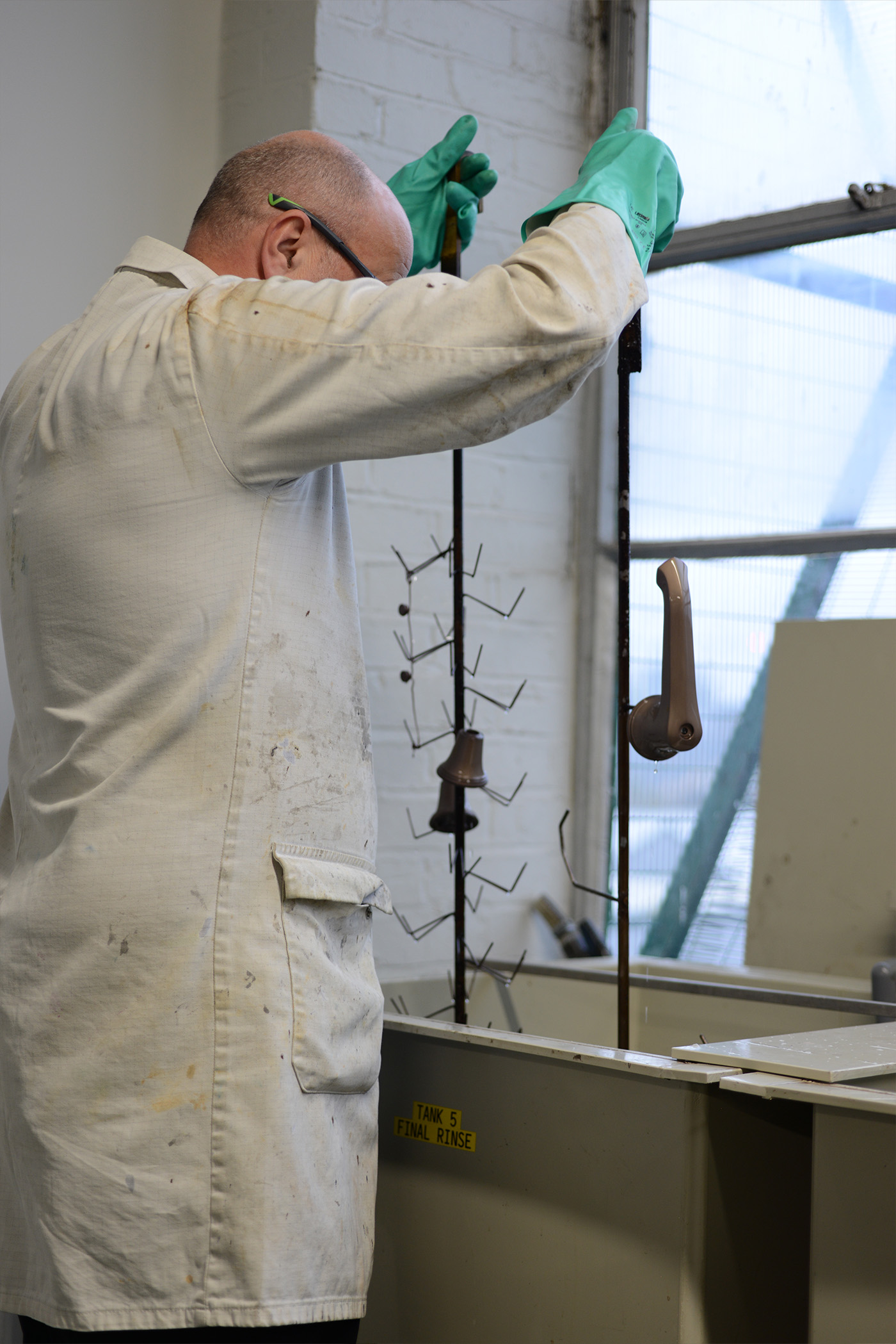 A professional lifting a basin tap and side valves on a jig from its final rinse bath