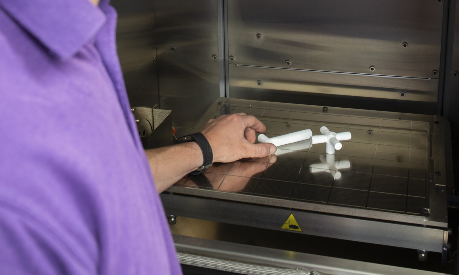 A manufacturing engineer picks up 3D prototypes from inside a carbon fiber machine.
