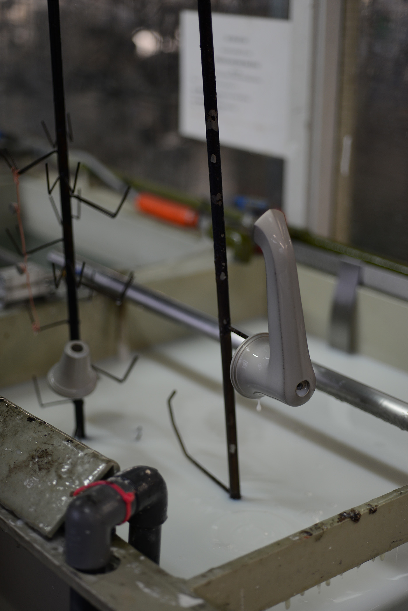 A basin spout and side valve parts on a jig being lifted from a lacquering solution bath