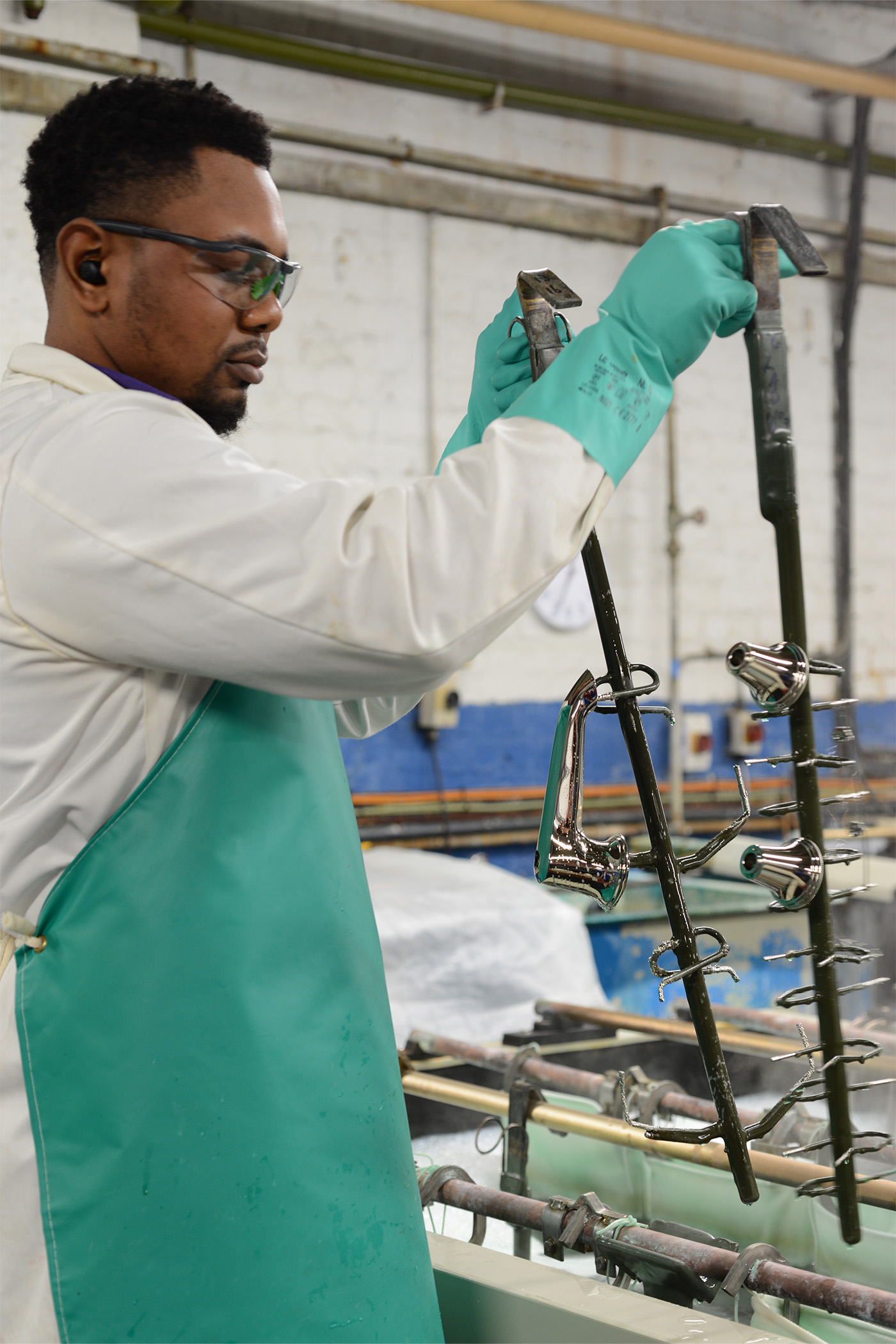 Up close of a person lifting a basin spout and side valve parts on a jig from cleaning solutions by hand