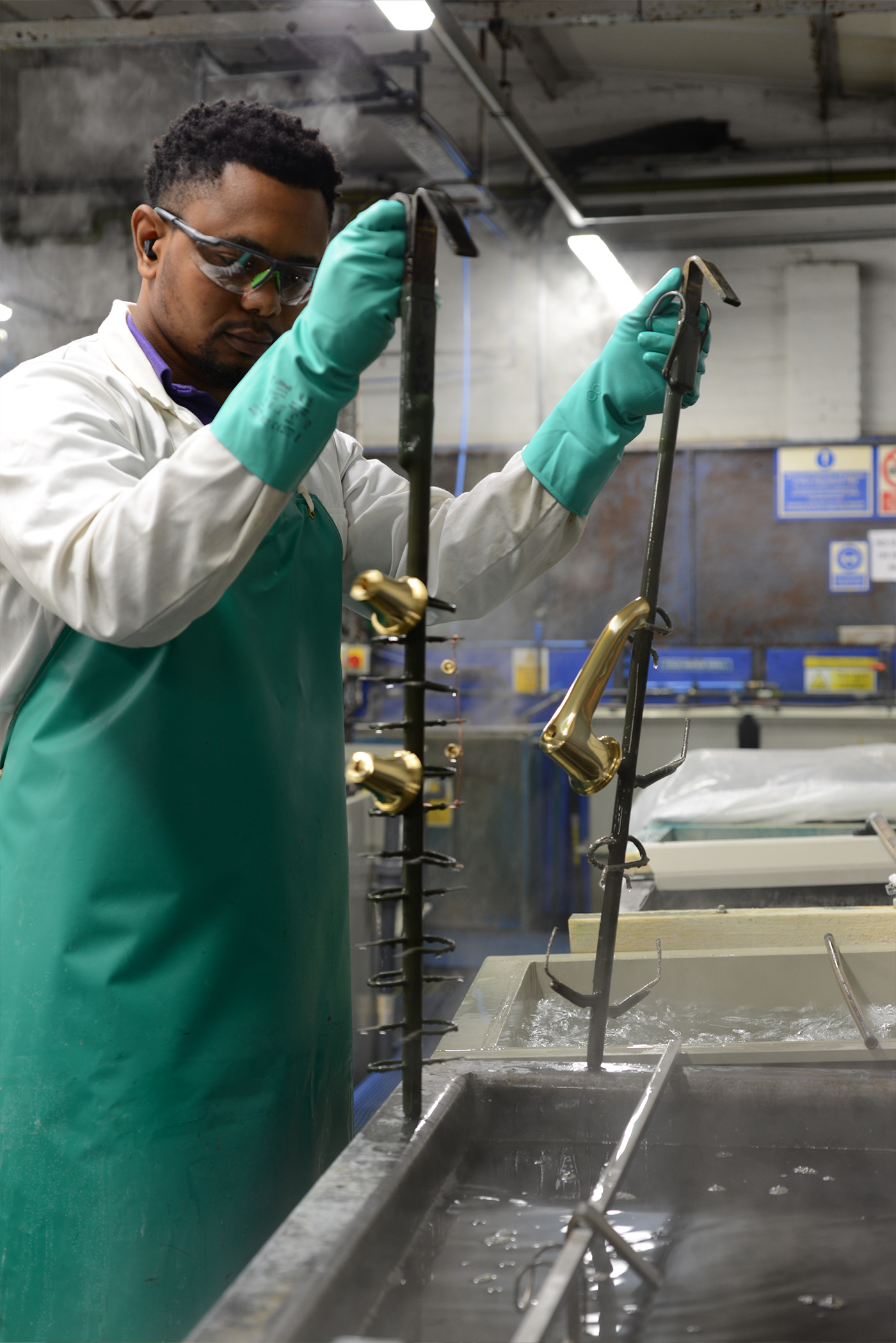 A person holding a jig with a basin spout and side valve parts dipping them in cleaning solutions